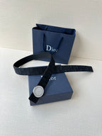 Dior belt laid across blue gift boxes, dark monogram strap with round buckle
