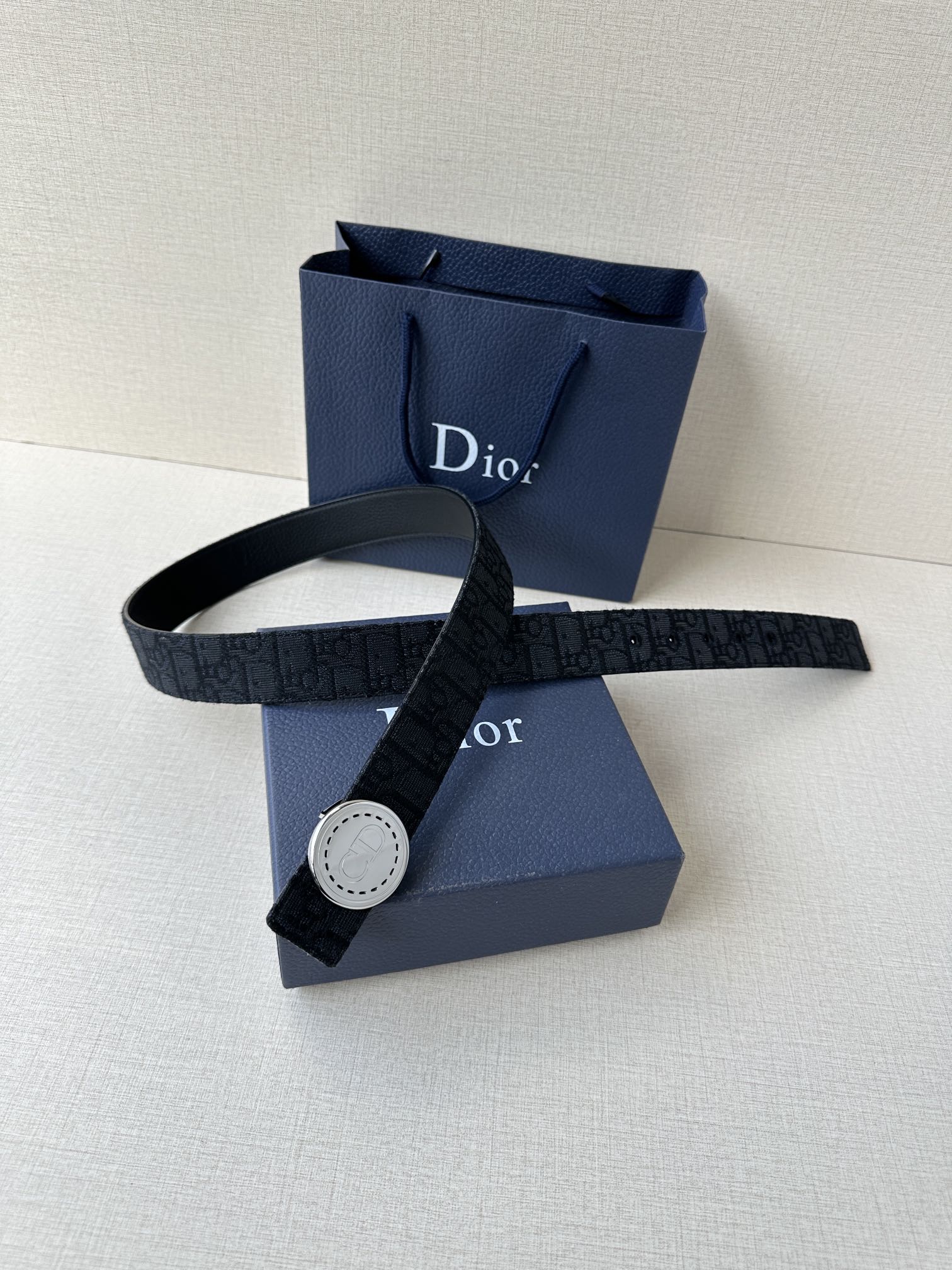 Dior belt laid across blue gift boxes, dark monogram strap with round buckle