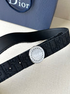 Dior belt close-up showing dark monogram strap and round silver-tone logo buckle