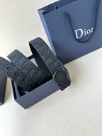 Dior belt with dark monogram strap and round gray buckle, stacked on blue box