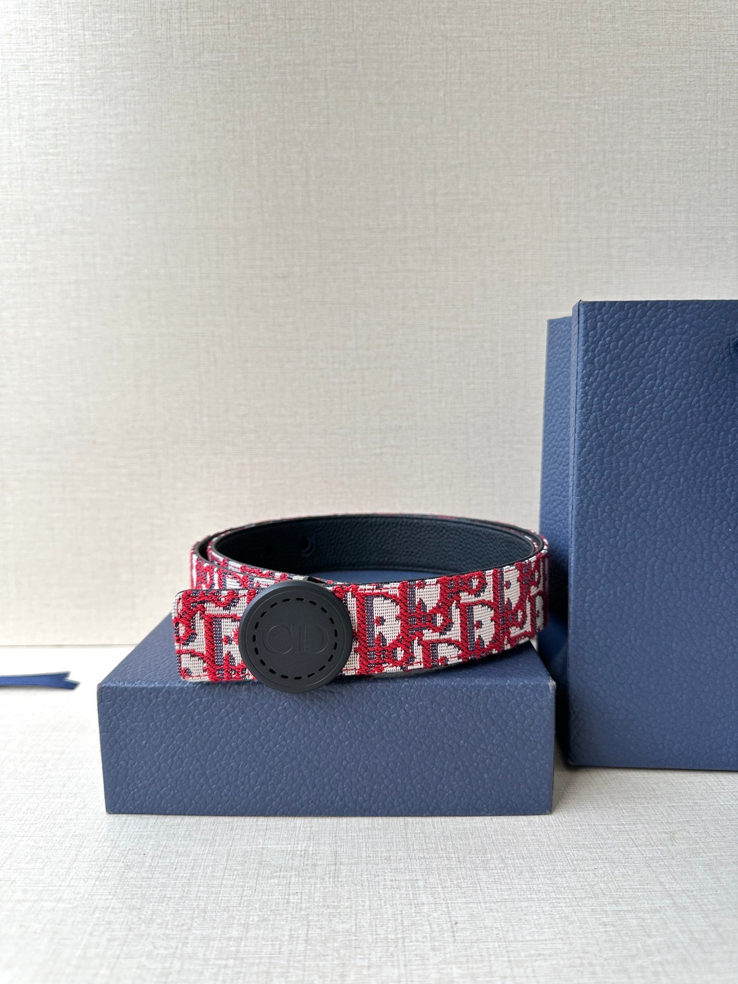 Dior belt on blue box; red-and-white monogram strap with round dark buckle