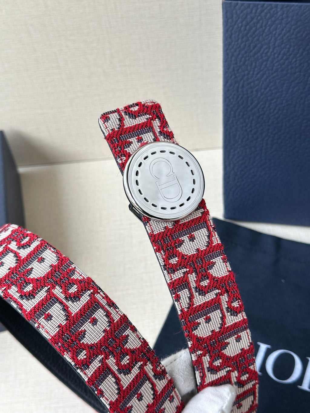Dior belt buckle detail: white circular hardware on red-and-white monogram strap