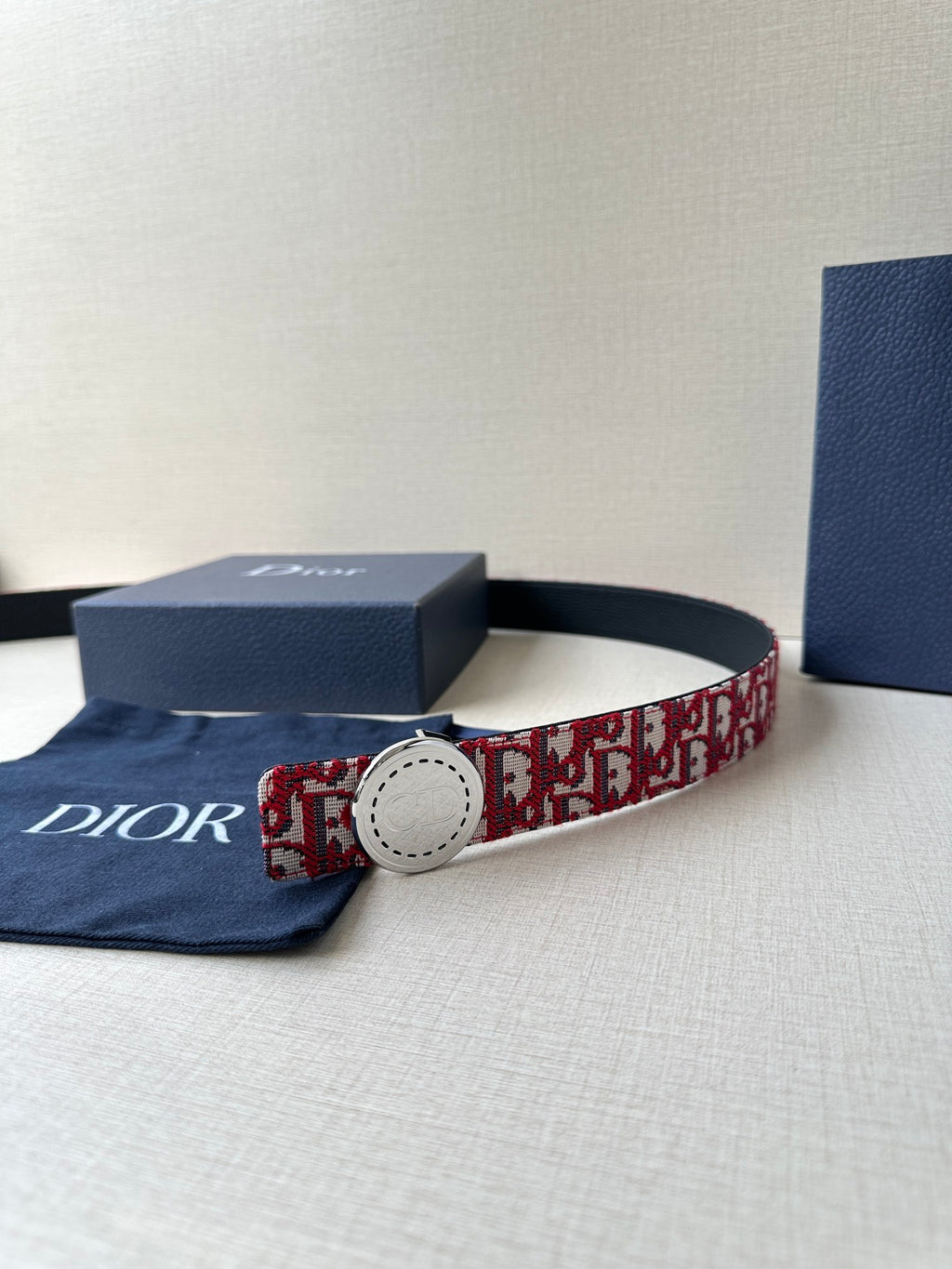 Dior belt on display; red-and-white monogram strap with white round buckle