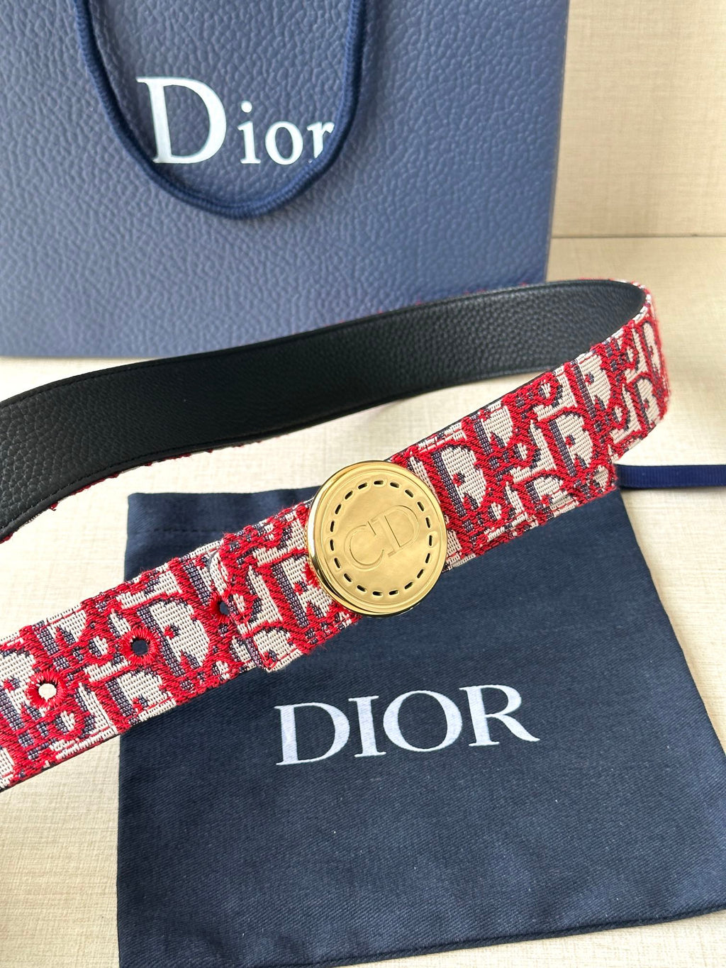 Dior belt close-up: red-and-white pattern strap with gold circular buckle and black trim
