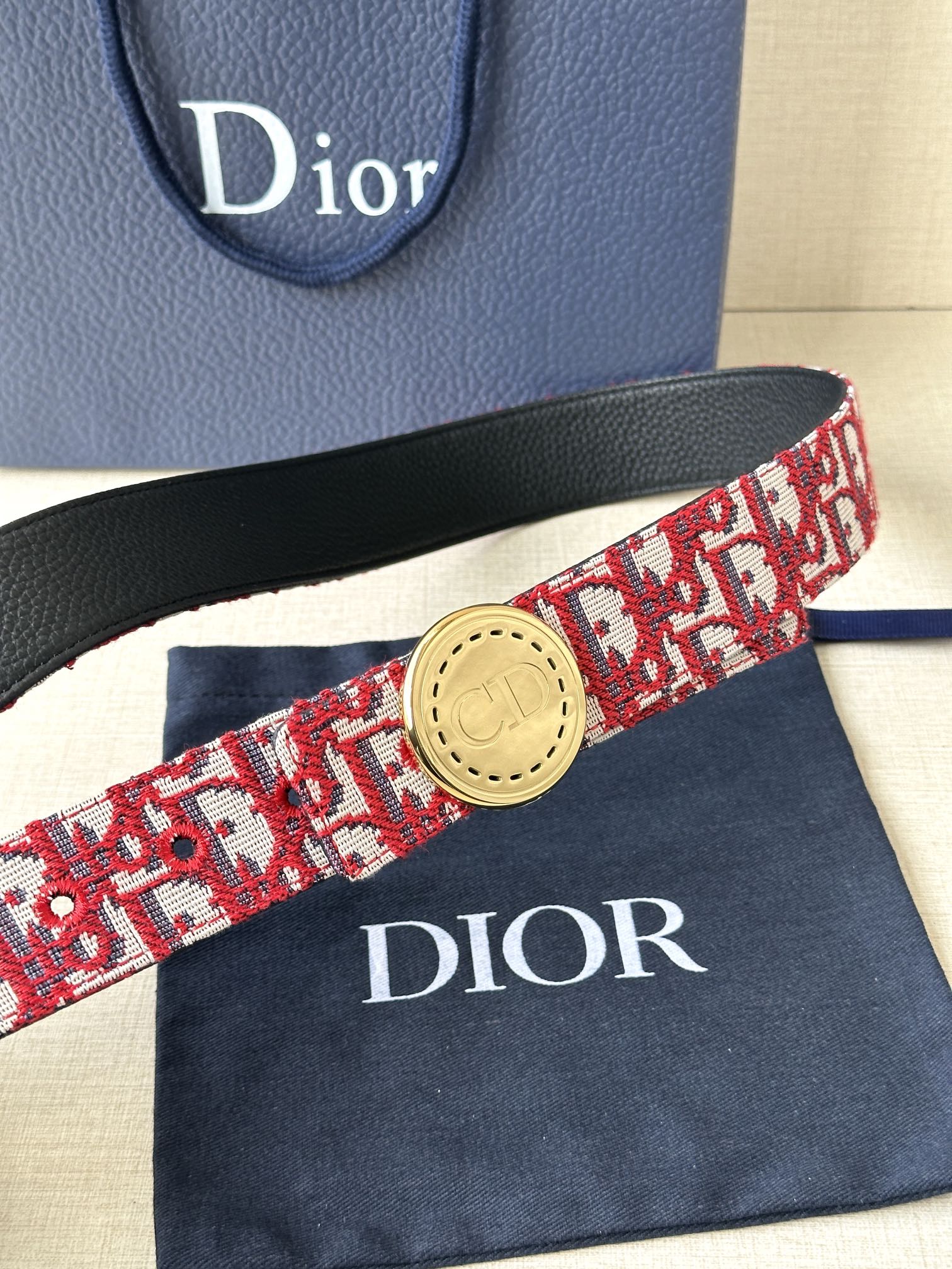 Dior belt close-up: red-and-white pattern strap with gold circular buckle and black trim