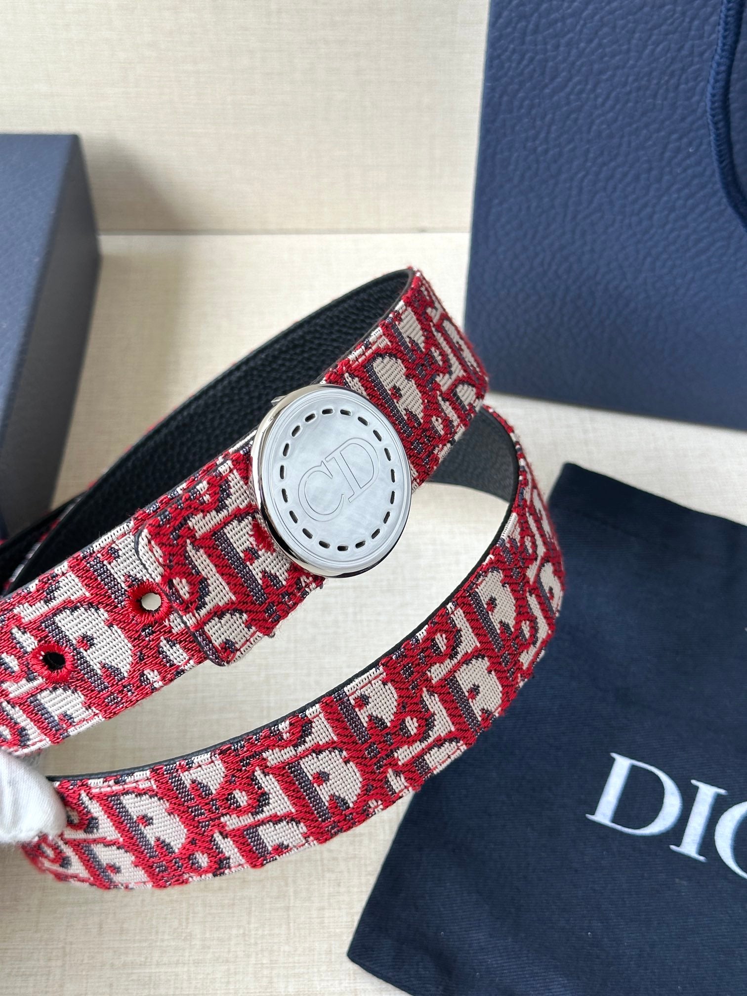 Dior belt close-up: red-and-white monogram strap with white circular buckle