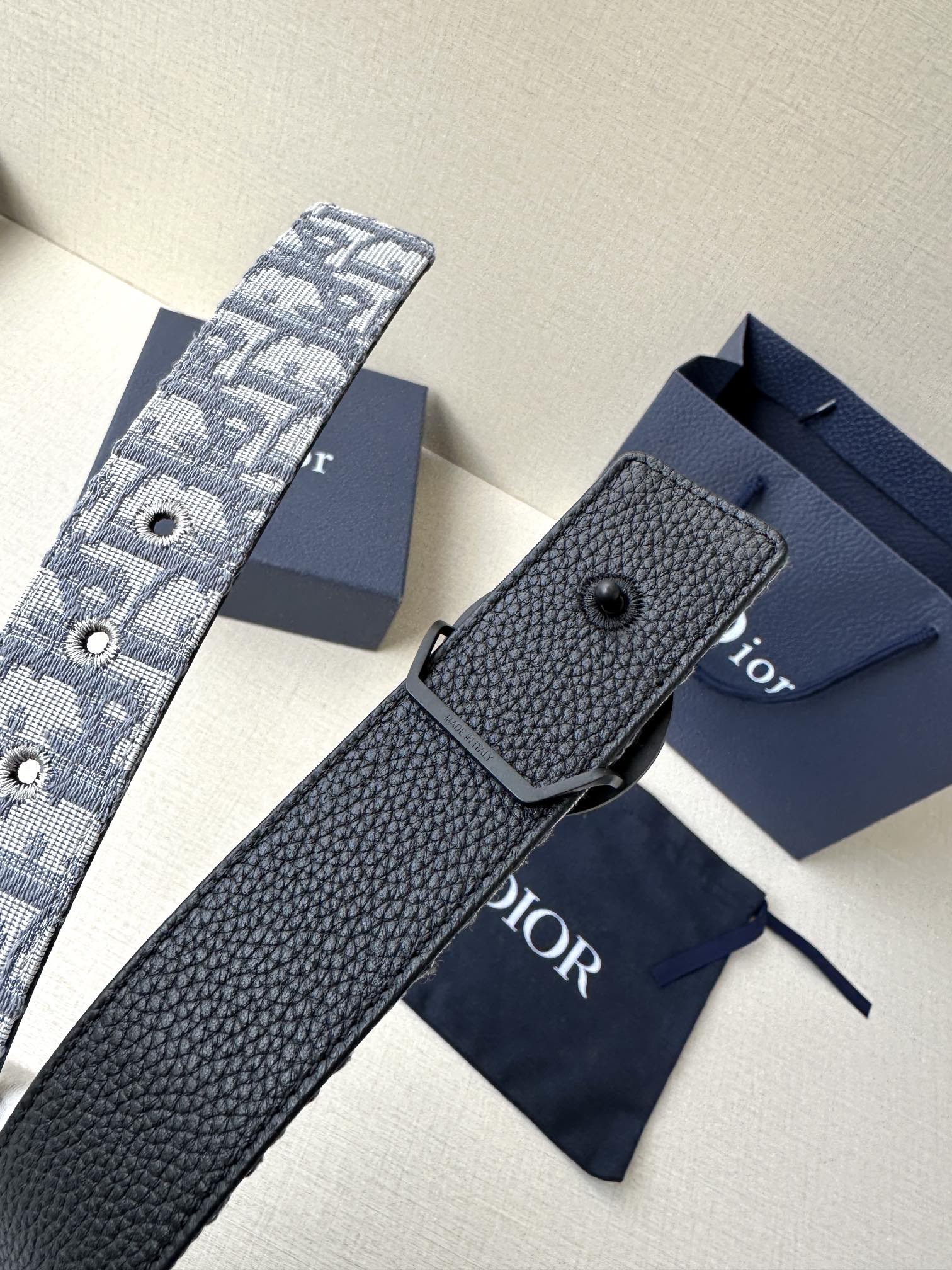 Dior belt with textured navy leather strap and dark keeper, laid on a box