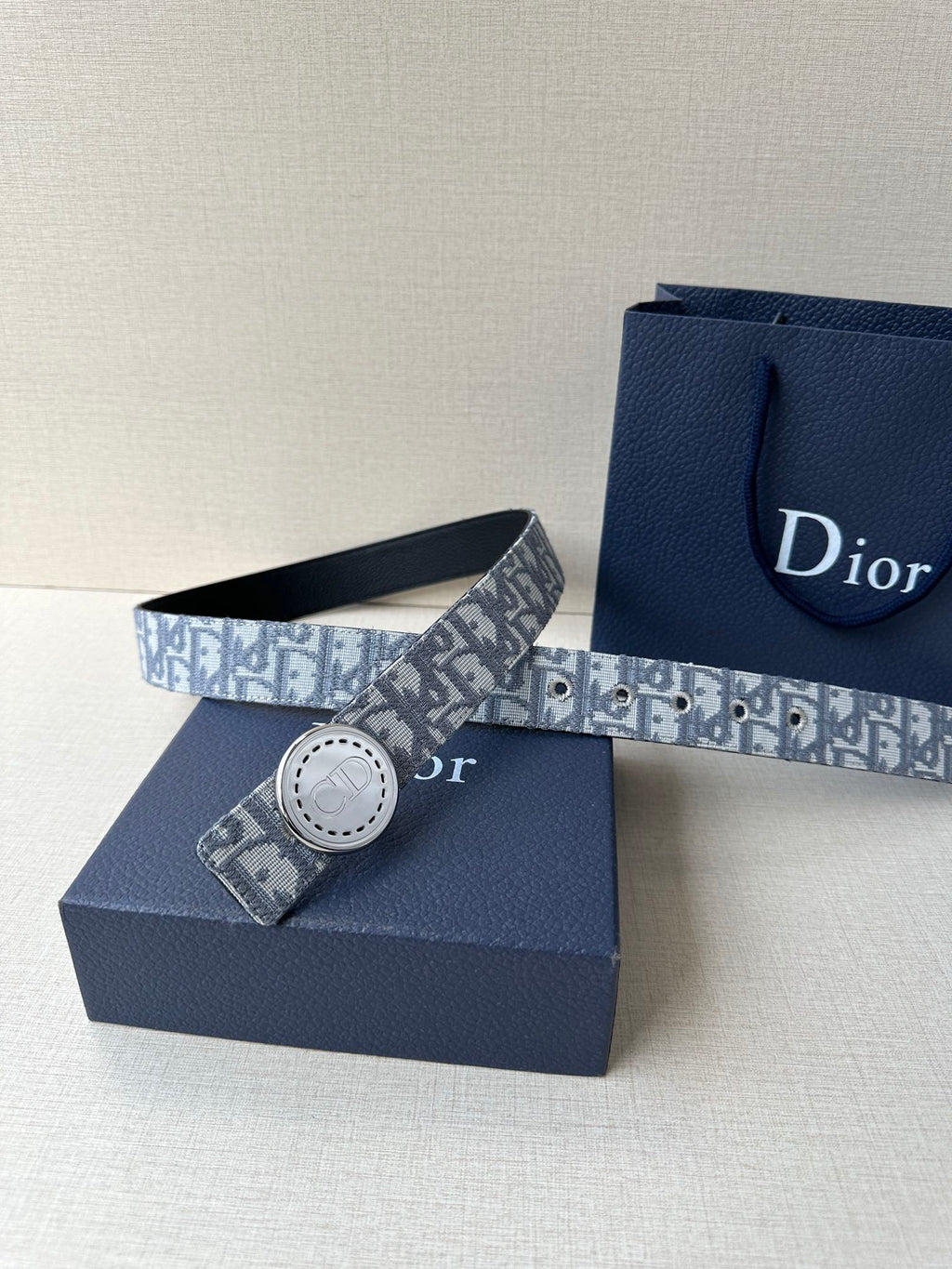 Dior belt with monogram strap and round silver-tone buckle beside gift box