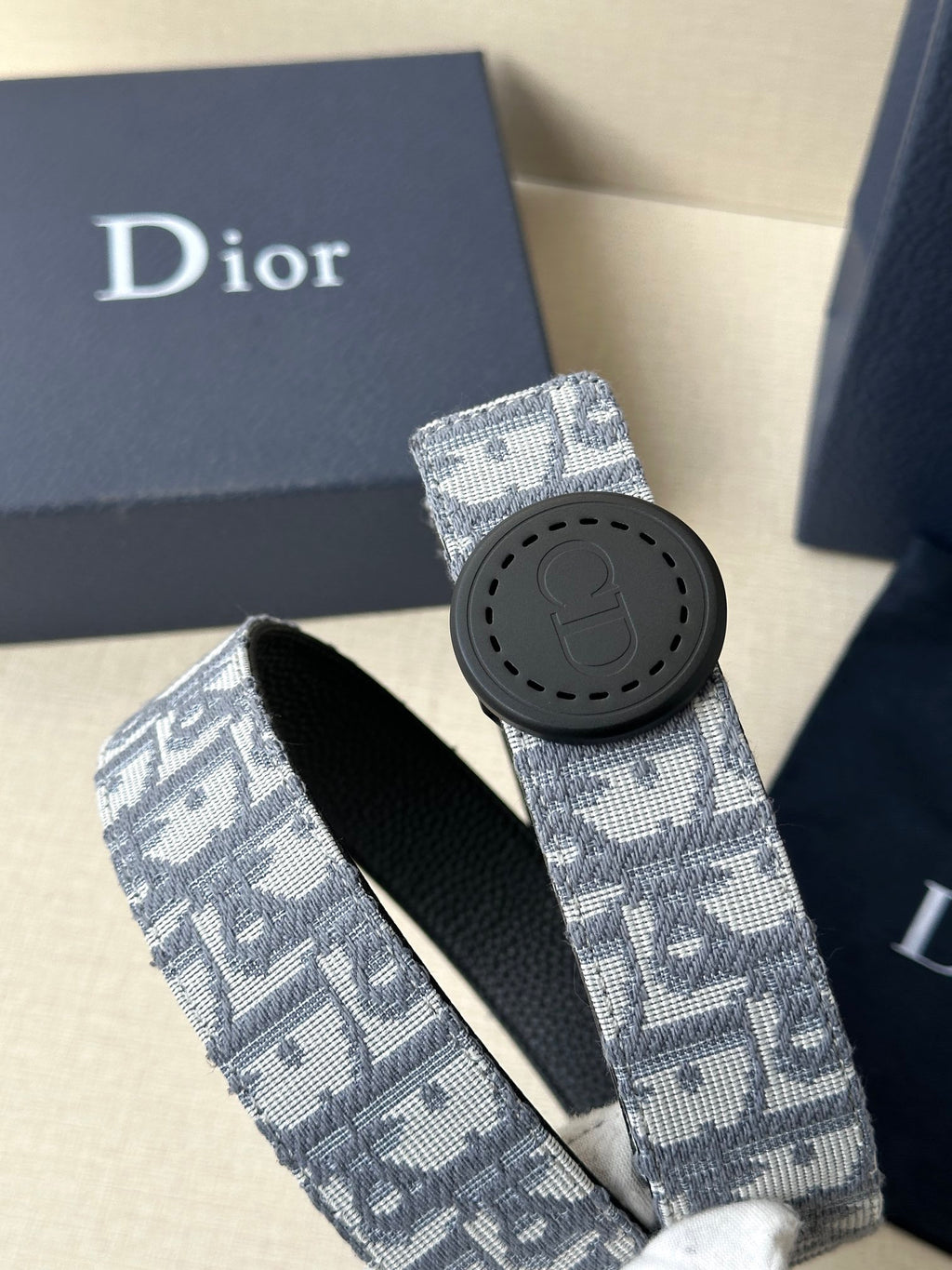 Dior belt with light blue monogram strap and dark round buckle with emblem
