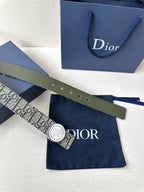Dior belt with monogram strap and round light buckle, styled on a blue gift bag.