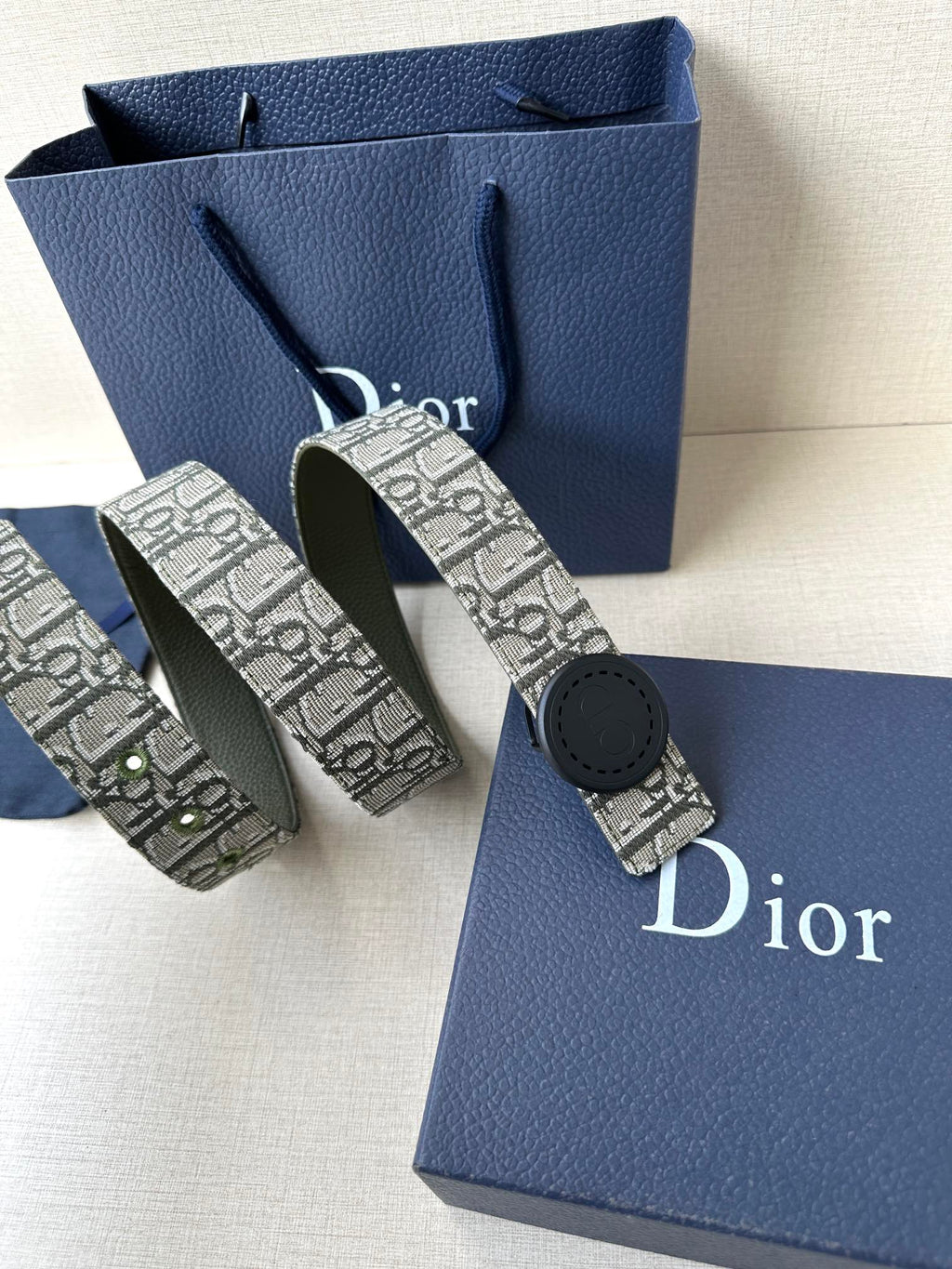 Patterned Dior belt with round black buckle, shown with matching belts beside gift bags.