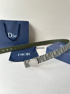 Dior belt with monogram fabric strap and circular pale buckle, laid across a box.