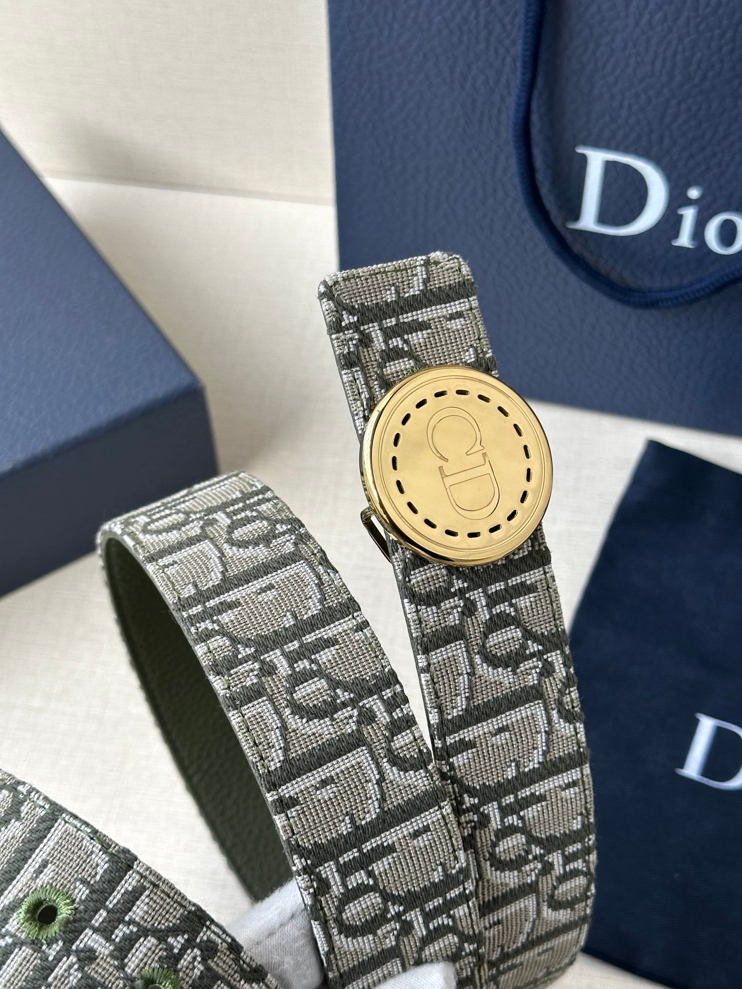 Dior belt close-up with monogram fabric and round gold-toned buckle.
