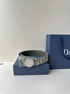 Dior belt with monogram fabric strap and round light buckle, resting on blue box.