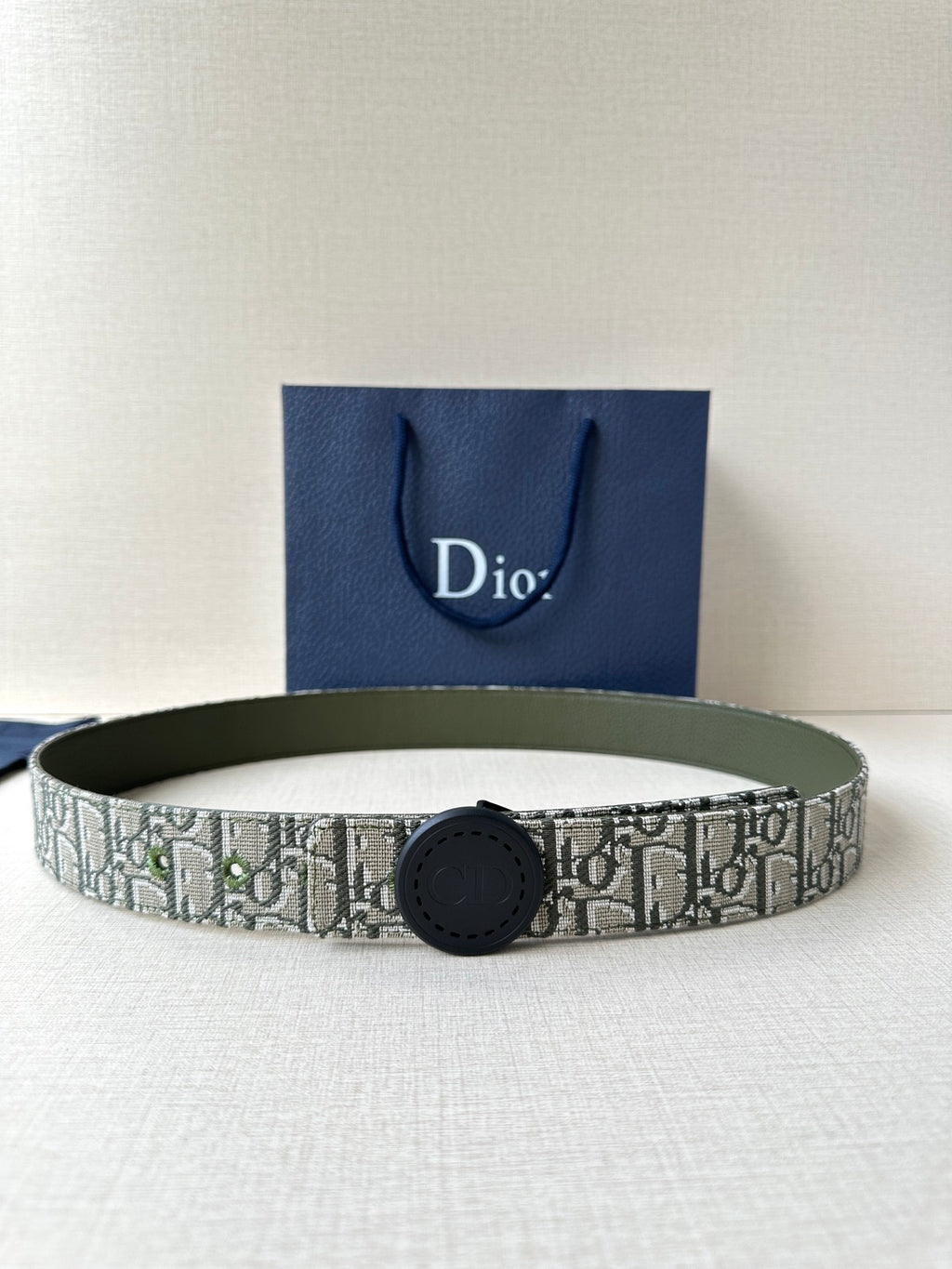Patterned Dior belt with round black buckle and olive-green leather backing.