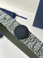 Dior belt close-up with round black buckle on monogram fabric strap and olive edge.