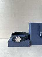 Navy Dior belt curled inside a box, featuring a round logo buckle
