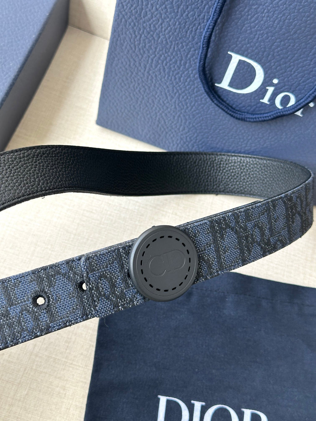 Navy Dior belt close-up with round logo buckle and perforation holes