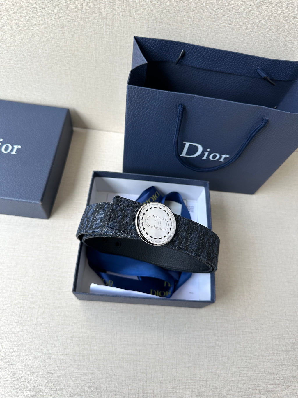 Navy Dior belt with round logo buckle in an open gift box