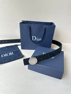 Navy Dior belt with round logo buckle laid across a blue Dior bag