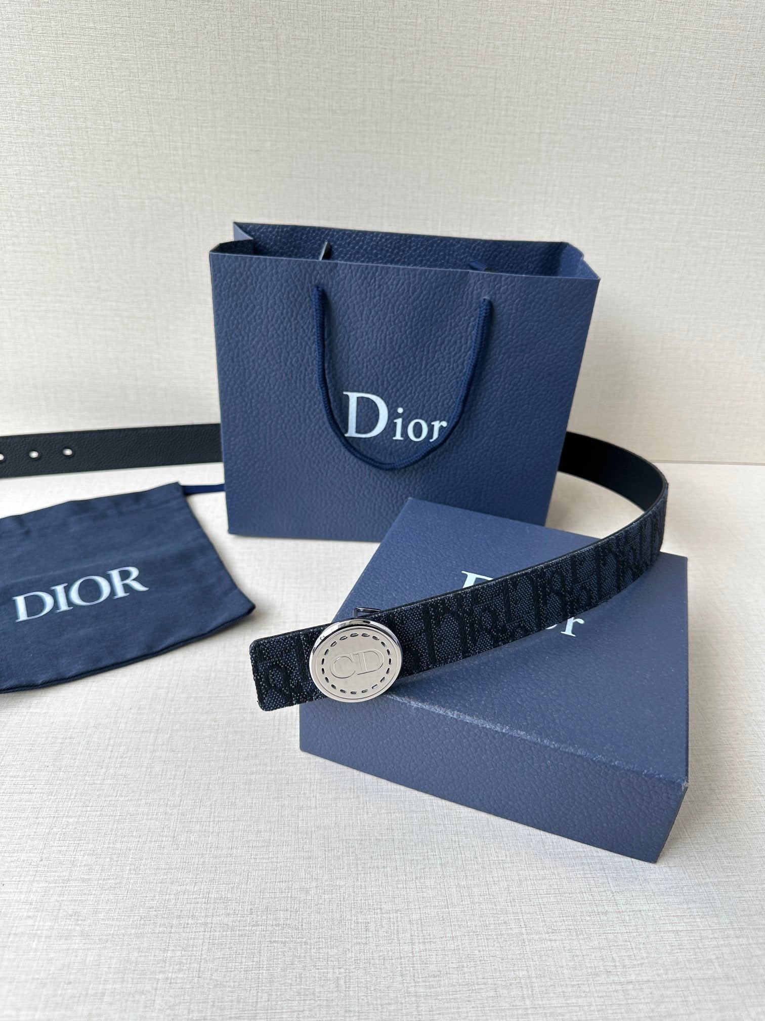 Navy Dior belt with round logo buckle laid across a blue Dior bag