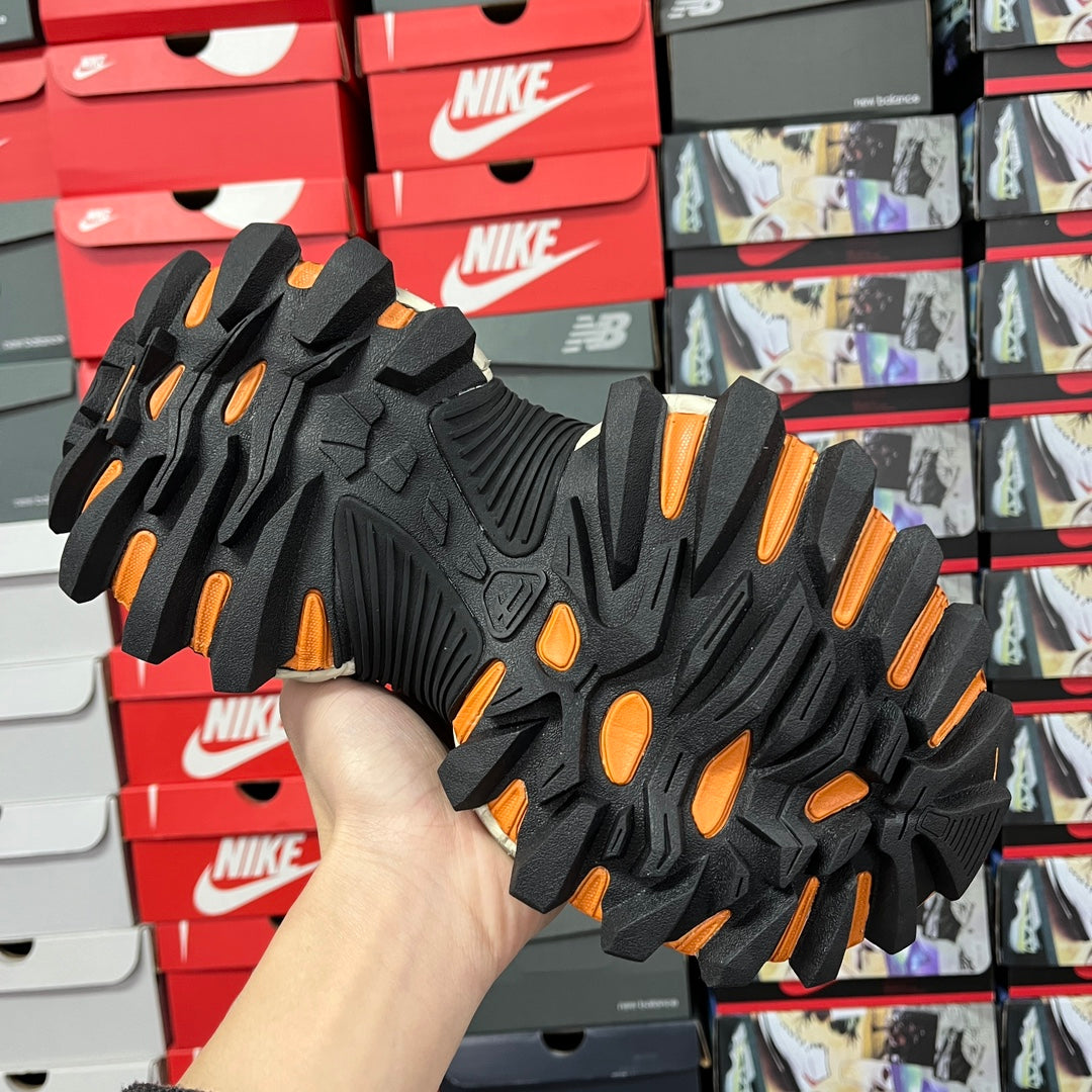 Balenciaga sneakers outsole view, black tread with orange traction highlights.