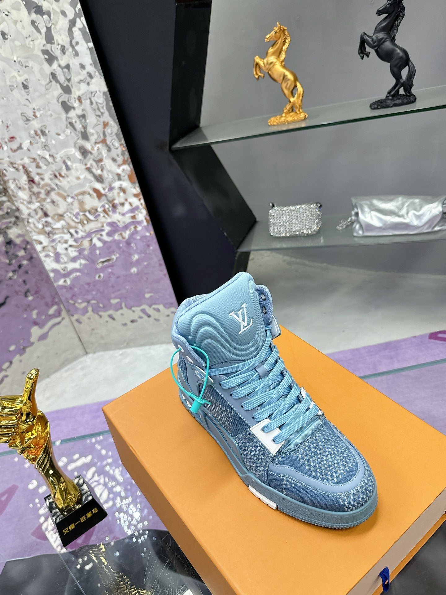 Single light blue high-top sneaker on orange box with teal lace detail and side emblem