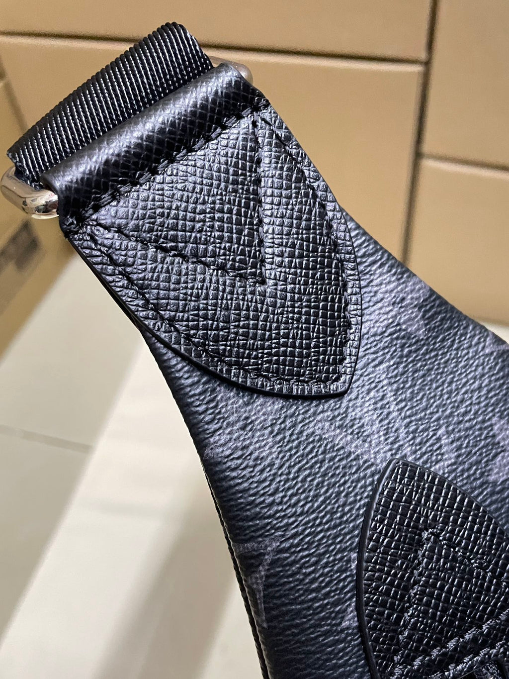 Pebbled leather flap detail on dark monogram crossbody bag