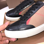 Burberry sneaker close-up, black lace-up upper with beige panel and red stripe, white sole.