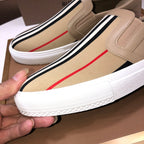 Beige slip-on sneaker close-up with striped band, red accent stripe, white sole