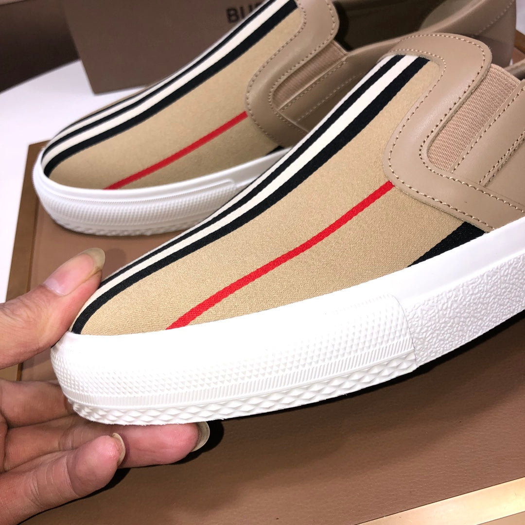 Beige slip-on sneaker close-up with striped band, red accent stripe, white sole