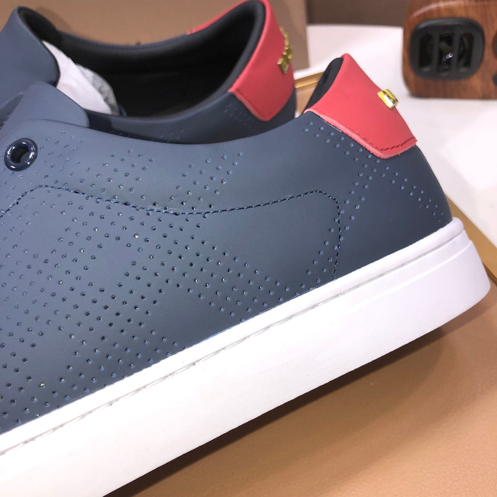 Burberry low-top sneaker side view, dark navy perforations and red heel tab with white sole.