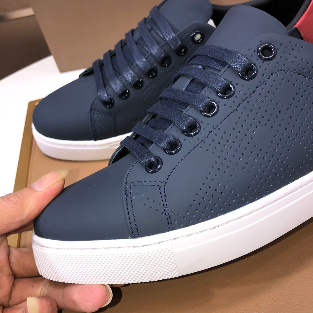 Burberry sneakers close-up: dark navy perforated lace-up with red heel tab and white sole.