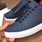 Burberry sneakers close-up: dark navy perforated lace-up with red heel tab and white sole.