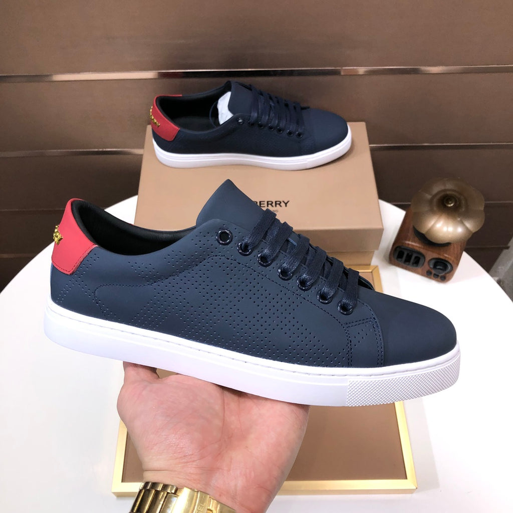 Burberry sneaker held in hand, dark navy with red heel tab and white rubber sole.
