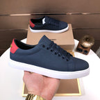 Burberry sneaker held in hand, dark navy with red heel tab and white rubber sole.