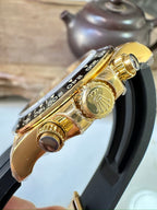 Rolex watch side view with gold case, crown and pushers, black rubber strap.