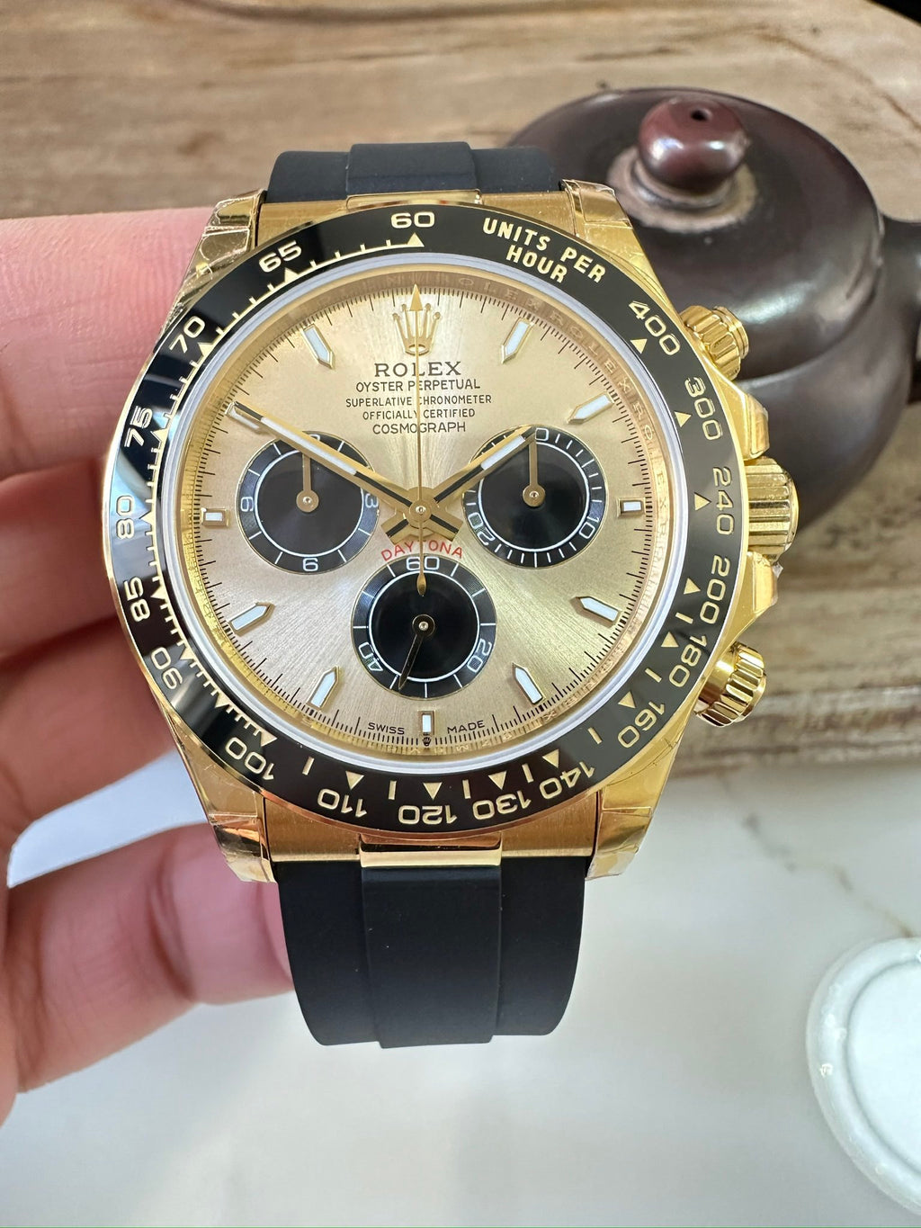 Rolex watch with gold case, black chronograph dial, gold bezel, black rubber strap.