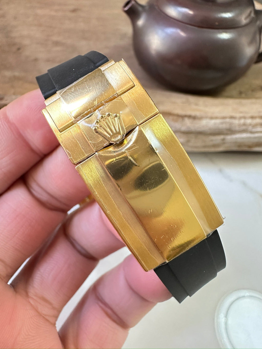 Rolex watch gold clasp and engraved buckle on black rubber strap.