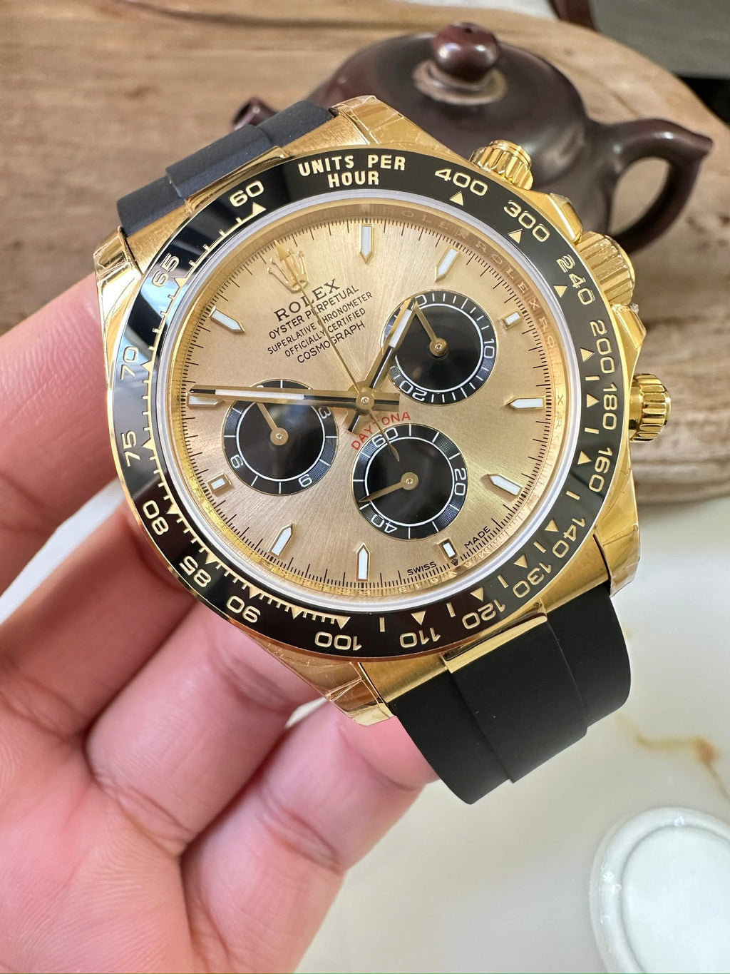 Rolex watch front view with gold bezel, black dial, three subdials, rubber strap.