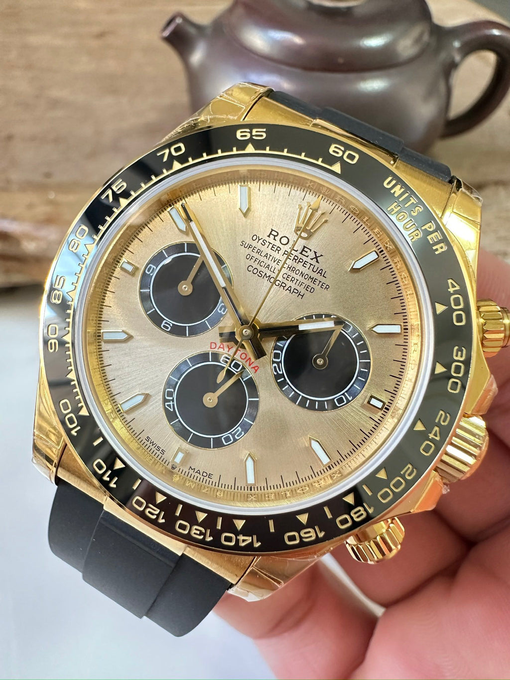 Rolex watch angled front view with gold bezel, black dial, three subdials, rubber strap.