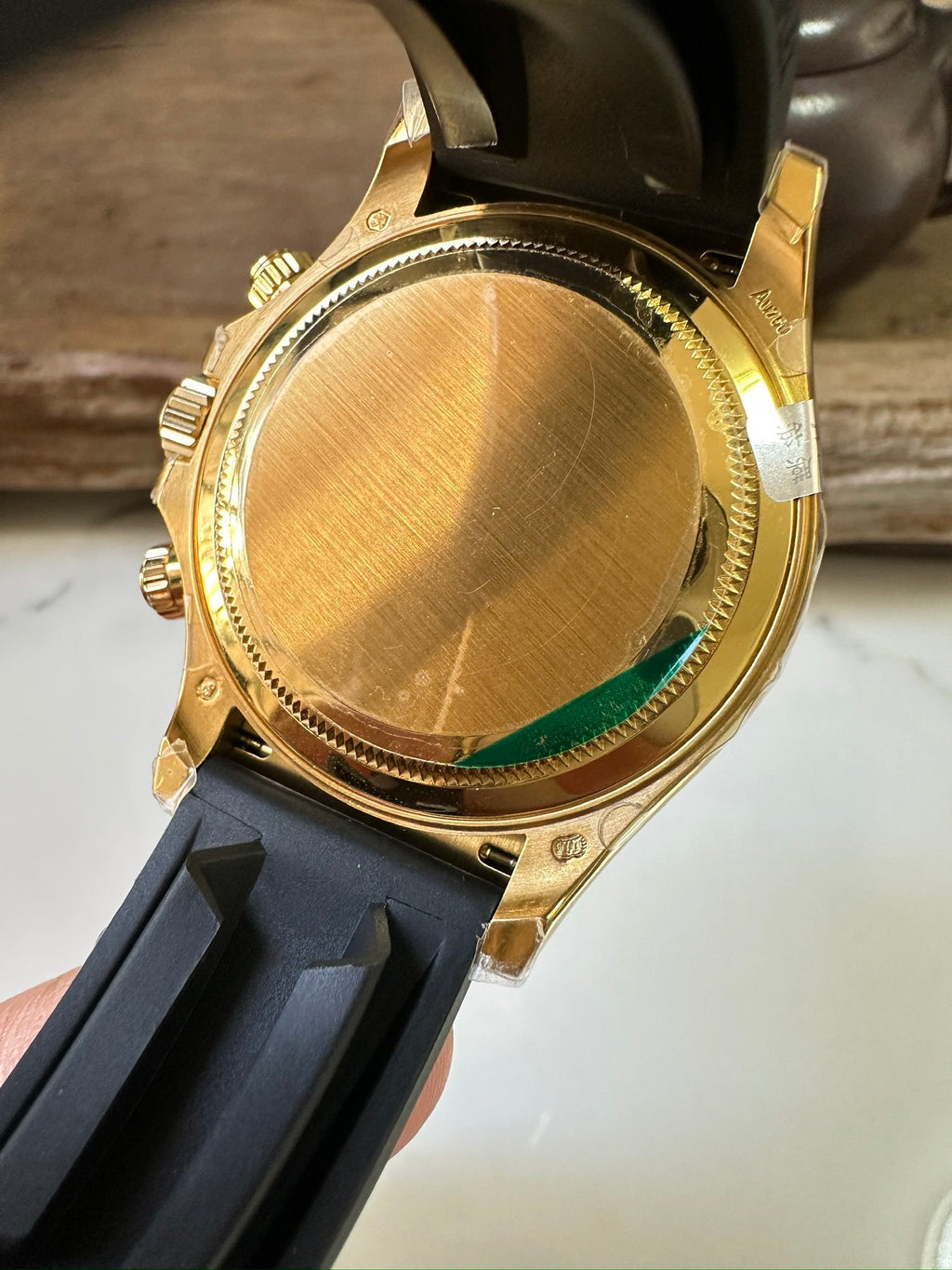 Rolex watch gold caseback with ridged bezel and small green glass on rubber strap.
