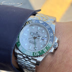 Rolex watch on wrist, white dial, blue bezel with green accents, steel bracelet