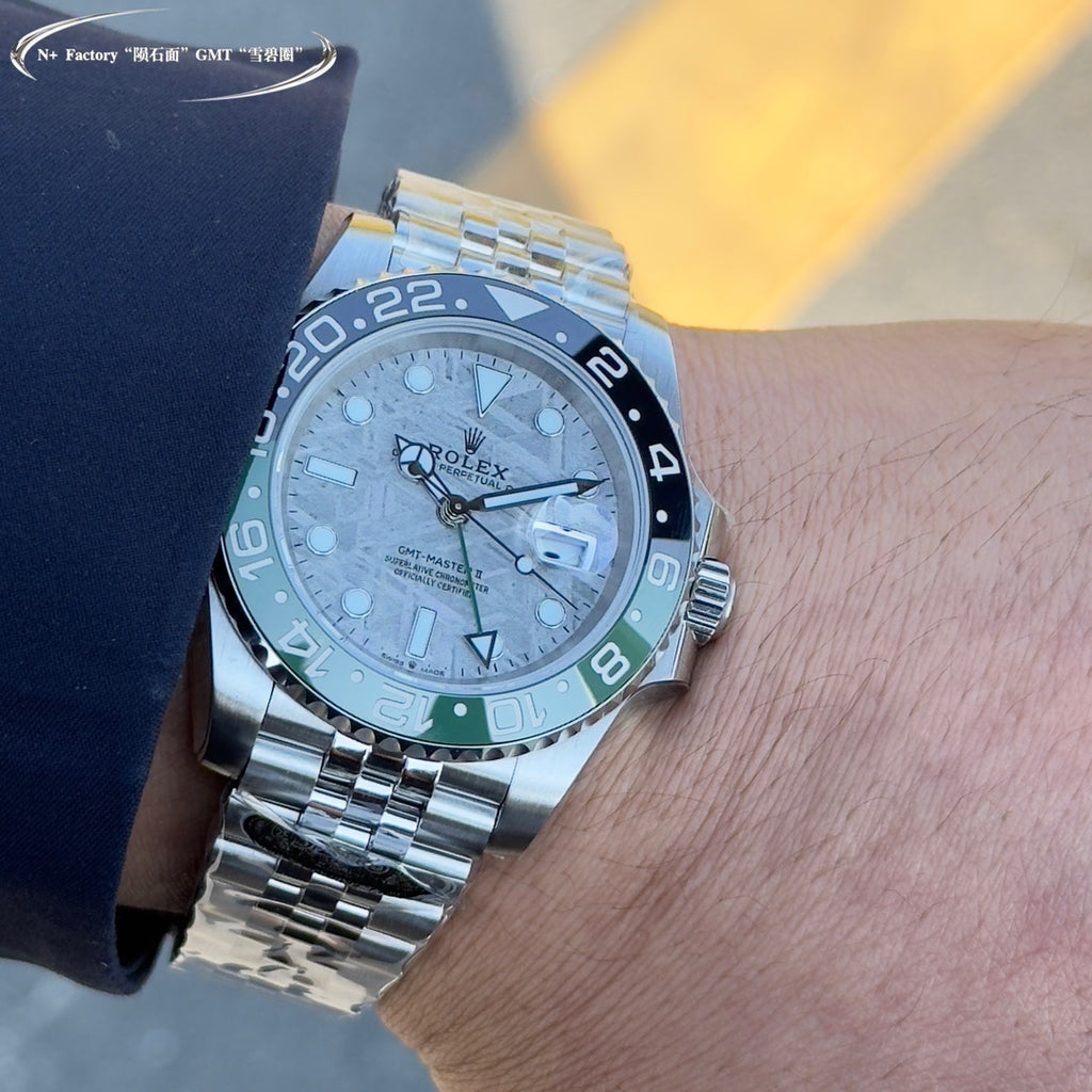 Rolex watch close-up on wrist, grey dial, blue bezel with green markings, steel bracelet