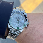 Rolex watch close-up on wrist, grey dial, blue bezel with green markings, steel bracelet