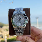Rolex watch centered on brown cushion, grey dial, blue-green bezel, steel bracelet