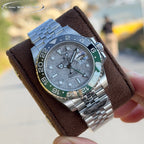 Rolex watch angled view, grey dial, steel bracelet, blue-green bezel on brown cushion