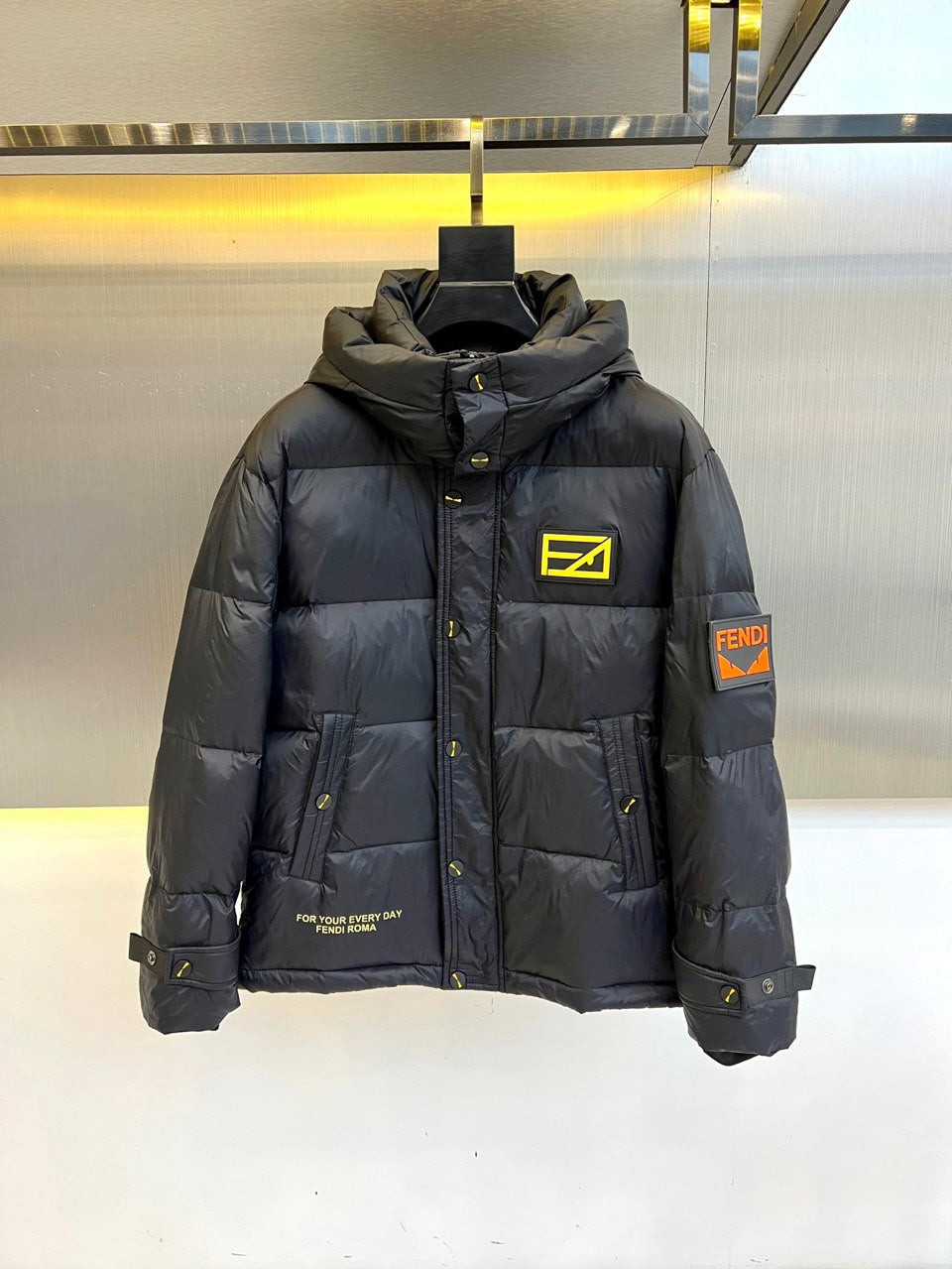 Dark puffer jacket with hood, front zipper, and yellow logo patch