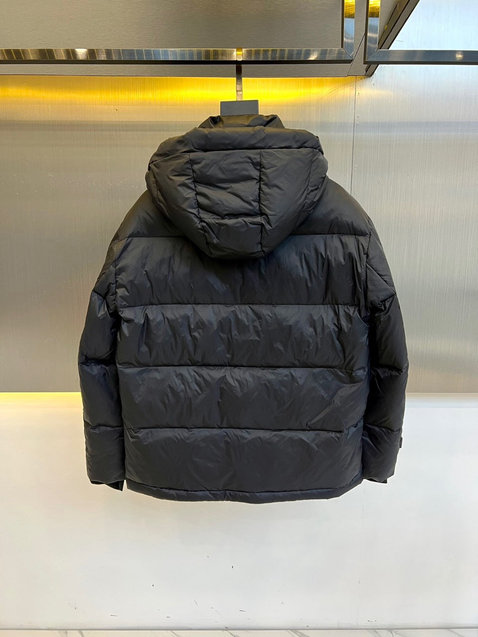 Dark hooded puffer jacket back view with horizontal quilting and logo hood trim