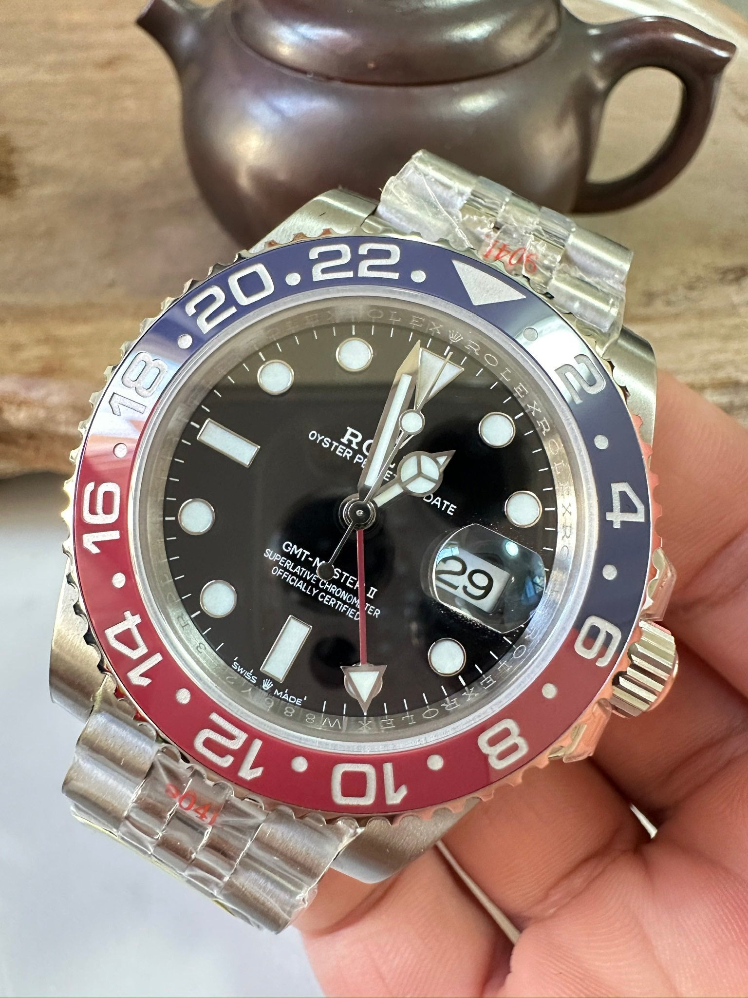 Rolex GMT watch front with black dial, blue/red bezel, metal bracelet and date